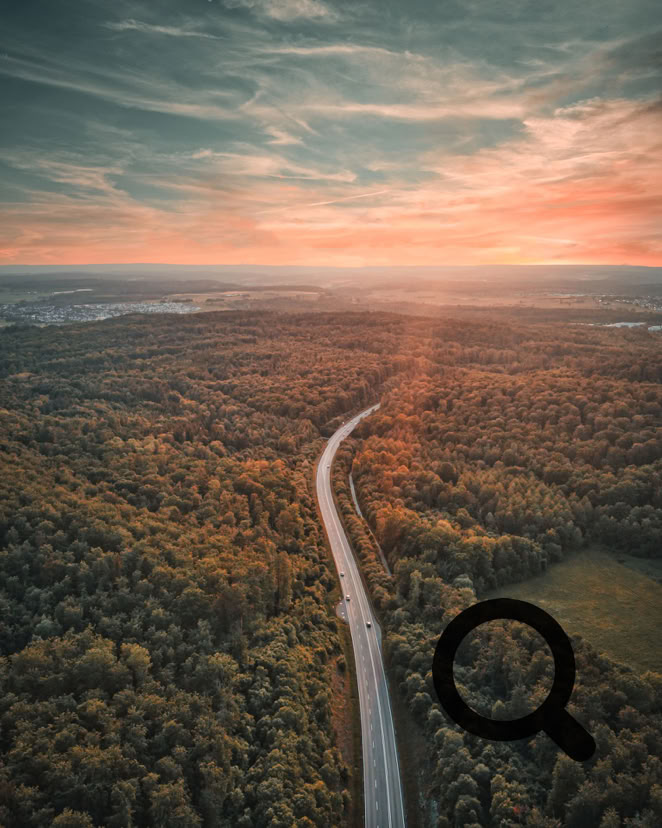 Stimmungsvolle Luftaufnahme eines einsamen Stra&szlig;enverlaufs durch einen dichten Wald bei Sonnenuntergang. Der Himmel zeigt warme Farben, die die Landschaft in goldenes Licht tauchen.